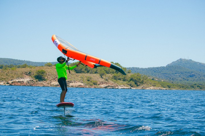 Person wingfoiling on water, wearing green shirt, with hills in the background.